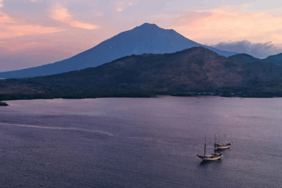 Indonesian phinisi sailing yachts, specifically the Silolona and Si Datu Bua, anchored in a serene bay at sunset.